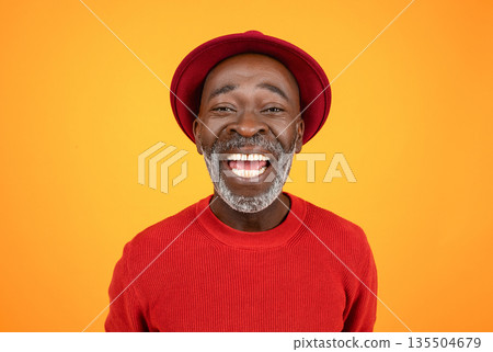 Happy excited senior african american man in hat and red clothes, with open mouth, look at camera, isolated on orange studio background, close up. Portrait, headshot for video call 135504679