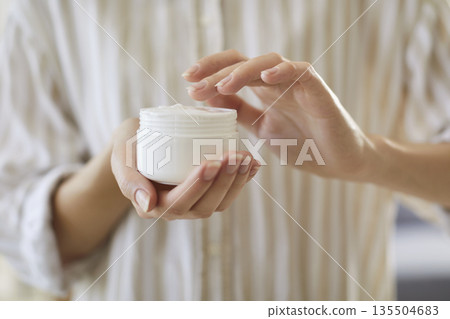 Close up view of female hands holding white jar with body cream Close up view of female hands holding white jar with body cream 135504683