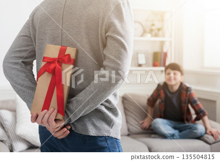 Father prepare gift case to impressed son sitting on sofa at home Father prepare gift case to impressed son sitting on sofa at home 135504815