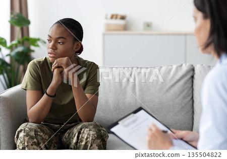 Portrait of black soldier woman having meeting with psychologist, african american female in military uniform sitting on the couch during therapy session, suffering depression, selective focus Portrait of black soldier woman having meeting with psychologist, african american female in military uniform sitting on the couch during therapy session, suffering depression, selective focus 135504822