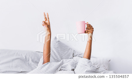 Happy morning. Hands of african american woman in blanket holds coffee, shows peace sign, panorama, free space Happy morning. Hands of african american woman in blanket holds coffee, shows peace sign, panorama, free space 135504857