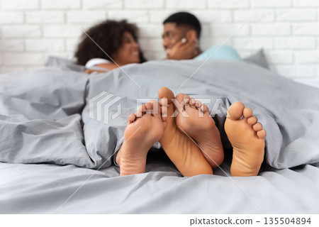 Young african-american couple relaxing in bed together, touching legs, barefoot feet on foreground, copy space Young african-american couple relaxing in bed together, touching legs, barefoot feet on foreground, copy space 135504894