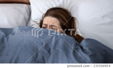 Mental health concept. Depressed young woman hiding under blanket on bed, suffering from depression, stress or insomnia. Unhappy lady feeling desperate or lonely, having psychological problem Mental health concept. Depressed young woman hiding under blanket on bed, suffering from depression, stress or insomnia. Unhappy lady feeling desperate or lonely, having psychological problem 135504954