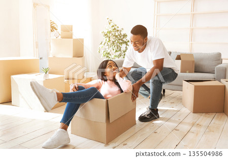 Black woman and her boyfriend playing together with cardboard box during relocation. Happy African American couple having fun in their new house on moving day. Panorama Black woman and her boyfriend playing together with cardboard box during relocation. Happy African American couple having fun in their new house on moving day. Panorama 135504986
