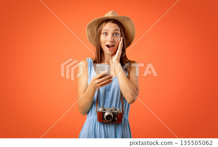 Shocked girl traveller with smartphone and camera on yellow studio background, amazing deals for tourists 135505062