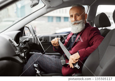 Driving safety concept. Senior businessman fasten seat belt in his car, ready to go to office. Aged man in stylish suit putting on his seatbelt before driving car to airport, copy space Driving safety concept. Senior businessman fasten seat belt in his car, ready to go to office. Aged man in stylish suit putting on his seatbelt before driving car to airport, copy space 135505117