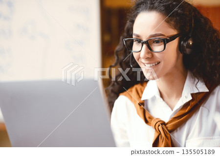 Professional Manager. Closeup portrait of confident woman wearing headset and eyeglasses, having videocall or online briefing on laptop computer, talking to colleagues or consulting client Professional Manager. Closeup portrait of confident woman wearing headset and eyeglasses, having videocall or online briefing on laptop computer, talking to colleagues or consulting client 135505189