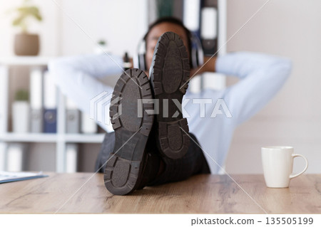 Resting black man shoes on workdesk in office, african american young businessman with headphones listening to music, leaning back, manager relaxing after difficult working day, empty space Resting black man shoes on workdesk in office, african american young businessman with headphones listening to music, leaning back, manager relaxing after difficult working day, empty space 135505199