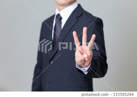 A middle-aged male businessman in a suit holding up three fingers 135505264