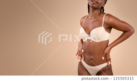 Young Black Slim Woman Posing In Underwear Over Beige Background, Enjoying Her Fit Body, Unrecognizable African American Female Standing In Lingerie And Touching Waist Cropped Image With Copy Space 135505315