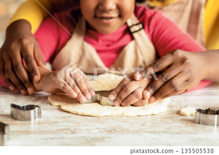 Closeup Shot Of Little Black Girl Cutting Out Heart Shape Of Dough While Baking With Mom In Kitchen, African American Family Mother And Daughter Enjoying Cooking At Home Together, Cropped Image 135505538