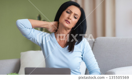 Exhausted Person. Portrait of tired mature lady sitting on the couch massaging sore neck, feeling pain after hard work, copy space. Adult woman suffering from inflammation, taking break at home 135505569