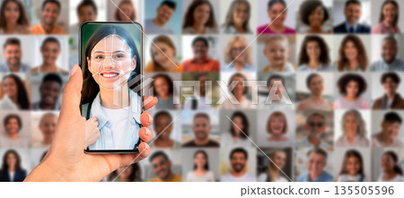 A hand holds a smartphone displaying a face recognition scan of a person. In the background, a collage of diverse faces emphasizes the application of identification technology today. 135505596