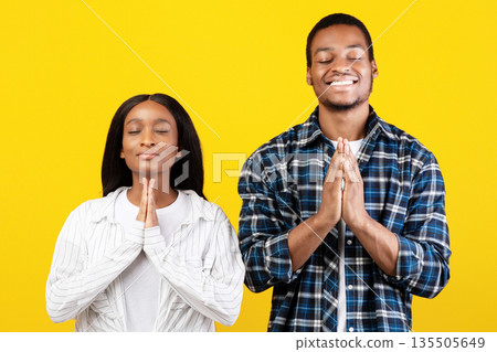 Pray, ask for fulfillment of desire and very want something. Smiling young african american family folded their hands and believe in dream, isolated on yellow background, studio shot, free space 135505649