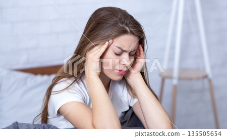 Depressed young woman massaging her temples to ease headache or stress in bed. Millennial lady suffering from sleep deprivation, mental disorder, overwhelmed with negative thoughts Depressed young woman massaging her temples to ease headache or stress in bed. Millennial lady suffering from sleep deprivation, mental disorder, overwhelmed with negative thoughts 135505654
