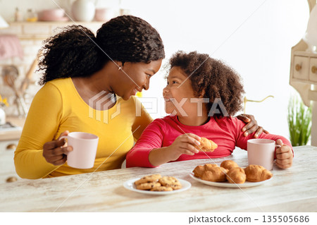 Loving Black Mom And Little Daughter Having Snacks In Kitchen, Enjoying Freshly Baked Croissants And Drinking Cocoa, Happy African Family Eating Homemade Pastry While Bonding At Home, Closeup Shot Loving Black Mom And Little Daughter Having Snacks In Kitchen, Enjoying Freshly Baked Croissants And Drinking Cocoa, Happy African Family Eating Homemade Pastry While Bonding At Home, Closeup Shot 135505686