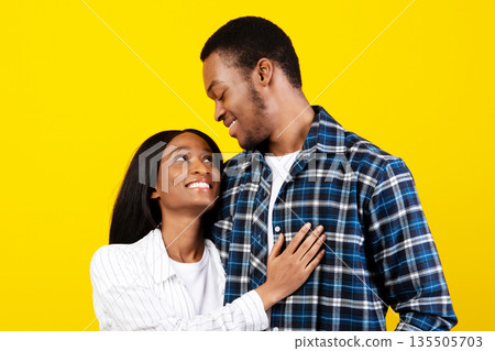 Tender moment, young romantic couple enjoying, married people have fun at date. Happy african american guy and lady hugs and looks at each other, isolated on yellow background, studio shot, free space 135505703