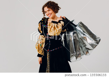Young adult smiling woman dressed in a medieval dress holding shopping bags in hands isolated white background 135506133