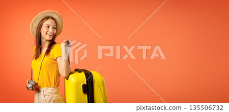 Smiling woman traveller with camera carrying suitcase and looking at copy space, yellow background Smiling woman traveller with camera carrying suitcase and looking at copy space, yellow background 135506732