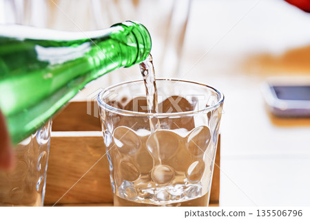 Mineral water being poured vigorously from a green bottle into a clear glass 135506796