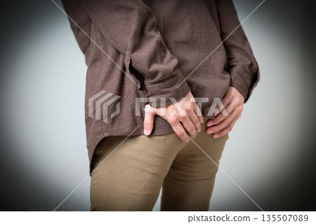 Middle-aged man suffering while holding his buttocks Middle-aged man suffering while holding his buttocks 135507089