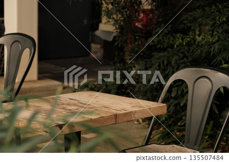 Cafe terrace seating, wooden table and antique-style chairs, sunlight filtering through the trees and greenery, background material Cafe terrace seating, wooden table and antique-style chairs, sunlight filtering through the trees and greenery, background material 135507484