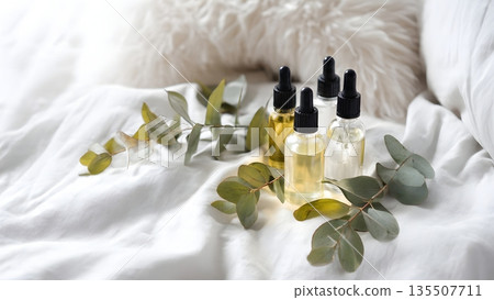 Eucalyptus leaves lie beside four transparent glass dropper bottles filled with golden serum on soft white fabric. AI Generated 135507711