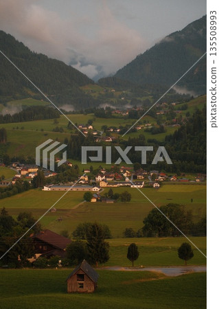 Scenic mountain landscape with lush green fields and quaint village nestled in valley 135508993