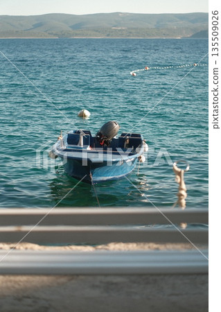Small blue boat floating on calm turquoise water with distant hills in the background 135509026