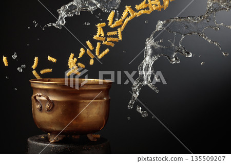 Vintage brass pot and pasta with a splash of water in motion. Vintage brass pot and pasta with a splash of water in motion. 135509207