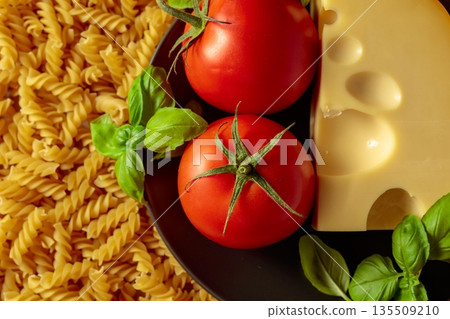 Uncooked fusilli pasta with tomatoes, basil and cheese. Uncooked fusilli pasta with tomatoes, basil and cheese. 135509210
