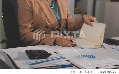 Close-up of businessman's hands making notes, mobiles, chart, desk, office 135510059