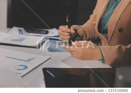 Close-up of businessman's hands making notes, mobiles, chart, desk, office Close-up of businessman's hands making notes, mobiles, chart, desk, office 135510060