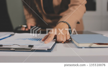 Close-up of businessman's hands making notes, mobiles, chart, desk, office 135510076
