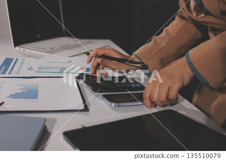 Close-up of businessman's hands making notes, mobiles, chart, desk, office 135510079