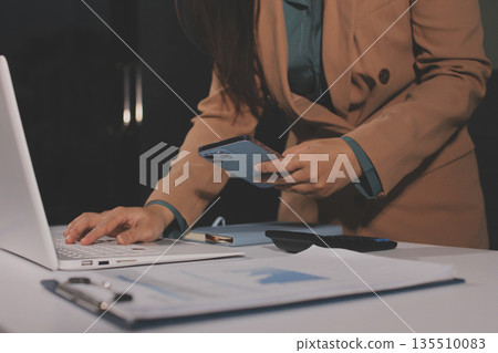Close-up of businessman's hands making notes, mobiles, chart, desk, office 135510083