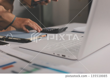 Close-up of businessman's hands making notes, mobiles, chart, desk, office Close-up of businessman's hands making notes, mobiles, chart, desk, office 135510085