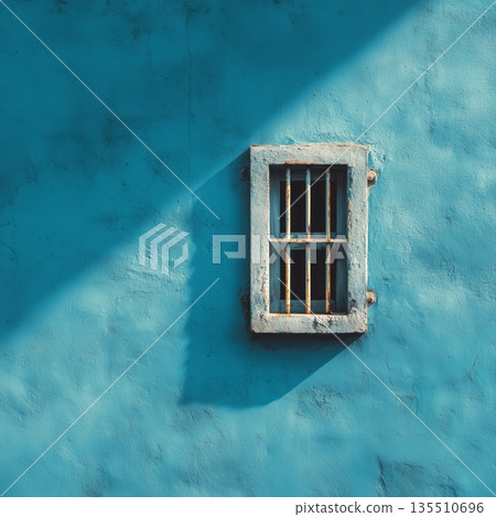 Unique blue wall with barred window highlights the play of light and shadow during the day in an urban setting 135510696
