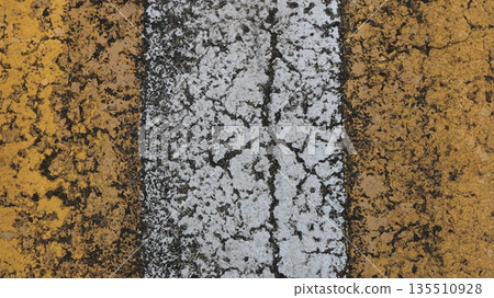 Vertical yellow and white stripe of painted asphalt with cracked rough texture, fragment of marked pedestrian crossing on road or highway in two colors, road background texture 135510928