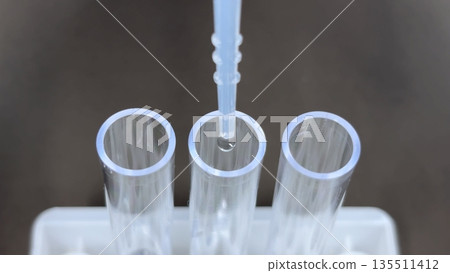 Close-up of a medical, testing, and experimental scene in which a dropper drips liquid into three plastic test tubes 135511412