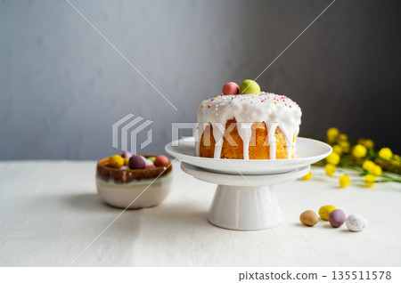 Easter festive cake with icing, sprinkles and eggs candy. White eggs and spring, yellow flower twigs. Easter festive cake with icing, sprinkles and eggs candy. White eggs and spring, yellow flower twigs. 135511578