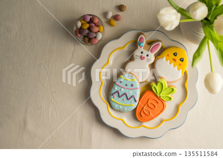 Easter festive colourful cookies bunny, carrot, egg, chick in a plate with egg candies and bouquet of spring tulips Easter festive colourful cookies bunny, carrot, egg, chick in a plate with egg candies and bouquet of spring tulips 135511584
