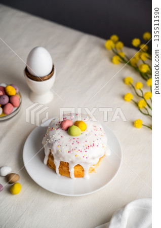 Easter festive cake with icing, sprinkles and eggs candy. White eggs and spring, yellow flower twigs. Easter festive cake with icing, sprinkles and eggs candy. White eggs and spring, yellow flower twigs. 135511590