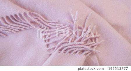 Pale pink cashmere scarf with fringe around the edge. Soft pink draped fabric texture. 135513777