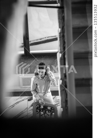 A woman thoughtfully sits on a staircase in St. Petersburg, gazing from a window, surrounded by a calming atmosphere and soft light. 135513932