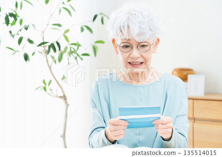 Senior woman thinking while looking at her bankbook Senior woman thinking while looking at her bankbook 135514015