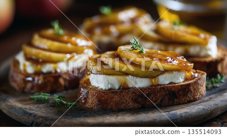 artisanal crostini appetizers: toasted bread slices topped with creamy white cheese, caramelized pear or apple, and a sweet honey glaze, garnished with fresh thyme on a dark wooden board. 135514093