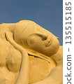 Close-up view of a monumental reclining Buddha statue in golden tones, symbolizing peace, mindfulness, Luang Pho Lokayasuttharam against a clear blue sky. 135515185