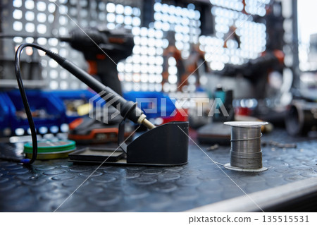 A soldering iron is resting on a worktable with a soldering iron and solder 135515531