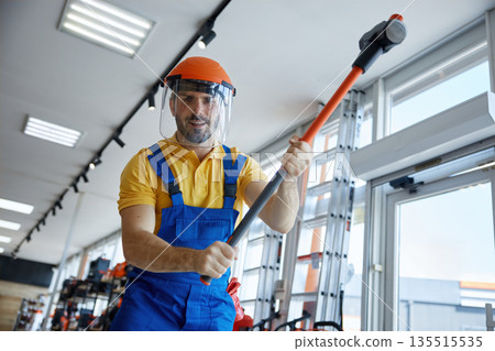 A man worker in overalls and a helmet is holding a hammerhead in a store 135515535